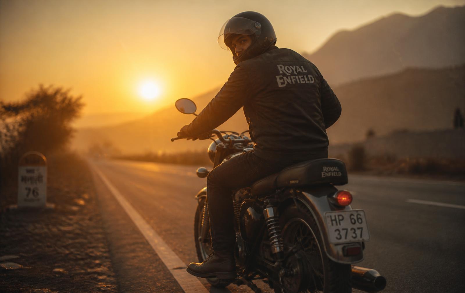 A lone motorcycle rider on an empty Indian highway at sunset